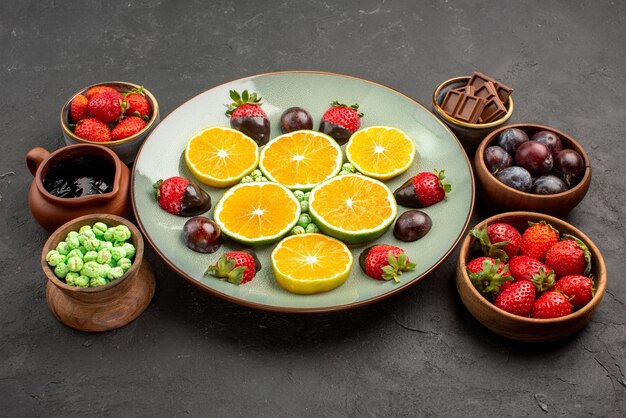 Frutti di vista laterale sul piatto fragole ricoperte di cioccolato e arancia tritata nel piatto bianco accanto alle ciotole di dolci e frutti di bosco in salsa di cioccolato sul tavolo