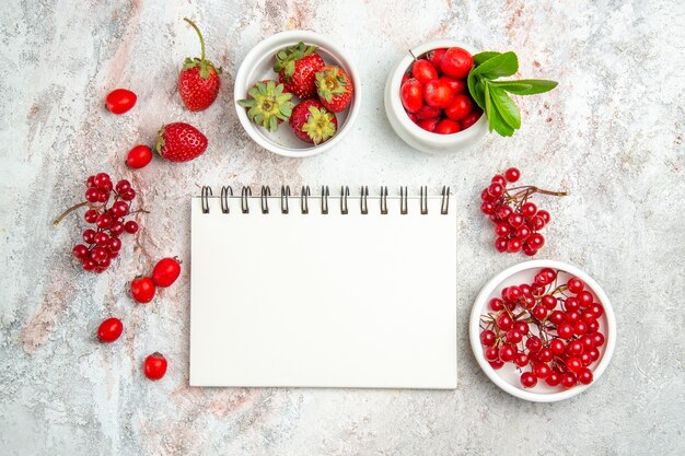 Frutti rossi di vista superiore con il blocchetto per appunti sulla frutta rossa della bacca della tavola bianca