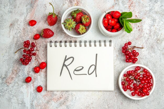 Frutti rossi di vista superiore con il blocco note scritto rosso sui frutti rossi della bacca della tavola bianca