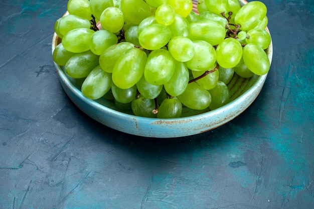 Frutti succosi pastosi dell'uva verde fresca di mezza vista superiore all'interno del piatto sullo scrittorio blu scuro.