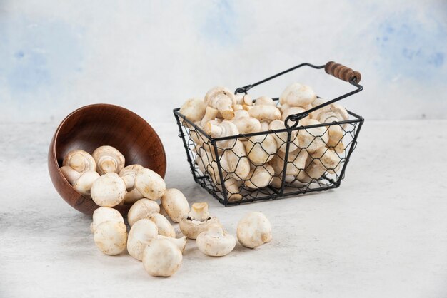 Funghi bianchi all'interno di una tazza di legno e di un cesto metallico.