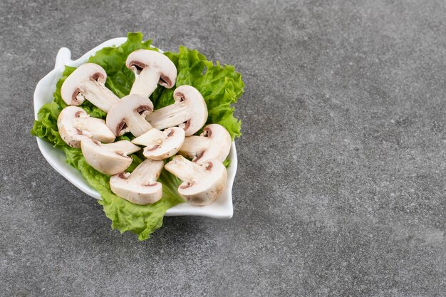 Funghi prataioli tagliati organici con lattuga sul piatto bianco.