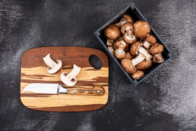 Fungo affettato con un coltello sul tagliere di legno vicino alla scatola di legno con i funghi freschi