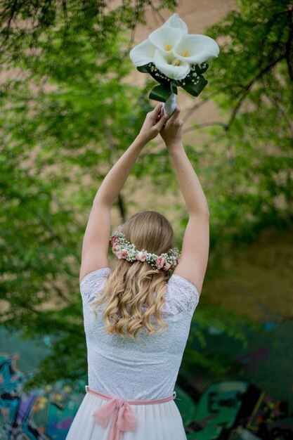 Fuoco poco profondo di una giovane sposa bionda che lancia un mazzo di fiori in un parco