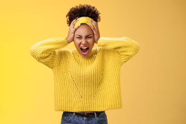 Furiosa indignata insana ragazza afro-americana impazzire urlando urlando sguardo aggressivo infastidito stufo di toccare la testa smorfie spaventoso pericoloso molto stressato, sfondo giallo.