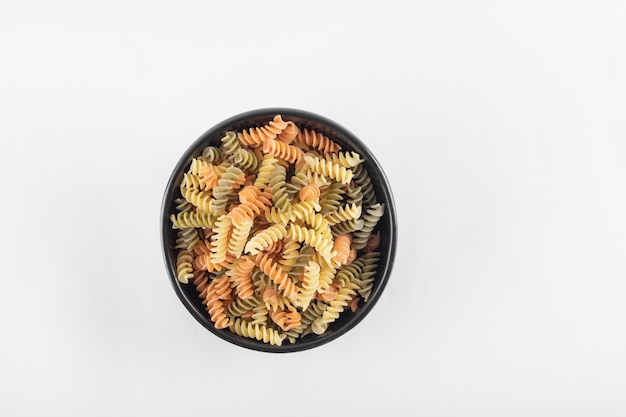 Fusilli colorati crudi in ciotola scura.