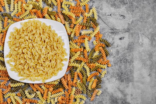 Fusilli colorati e ciotola di pasta cruda su sfondo marmo