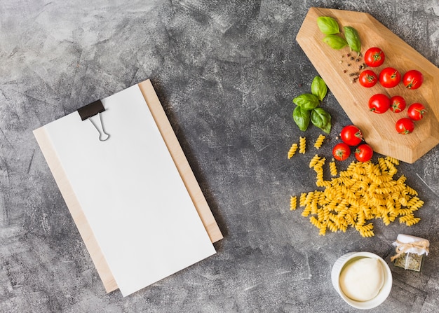 Fusilli crudo con ingredienti e carta bianca su appunti su sfondo grunge