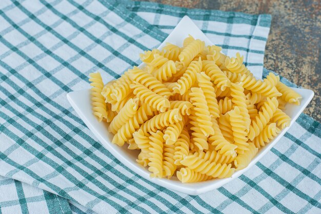 Fusilli pronti da cuocere in una ciotola su un asciugamano, sullo sfondo di marmo.