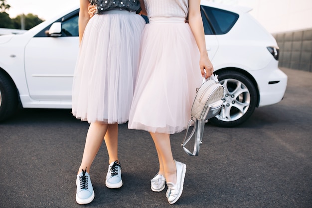 Gambe attraenti di modelle in gonne di tulle e scarpe da ginnastica su auto bianca.