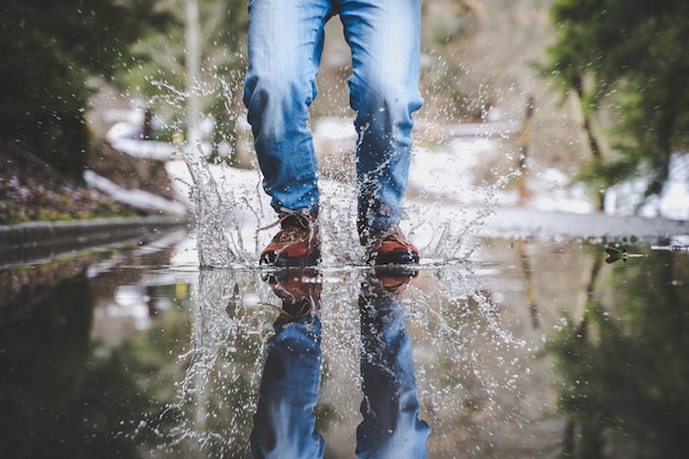 Gambe che indossano blue jeans e stivali marroni che camminano sulla strada bagnata