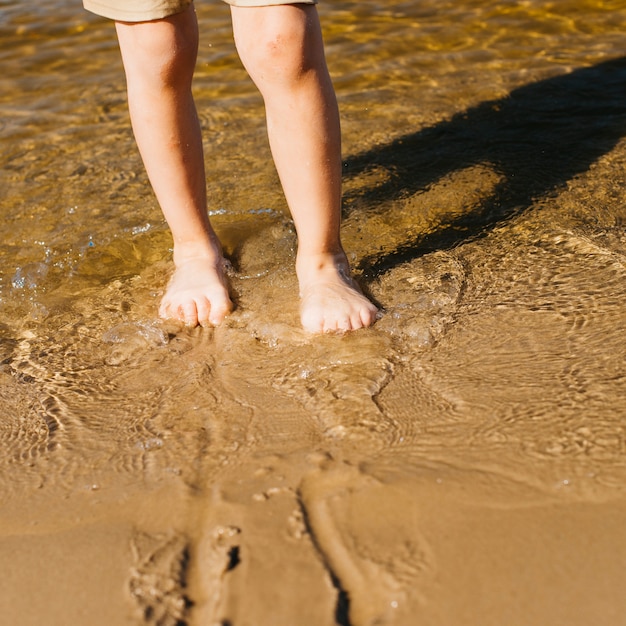 Gambe del bambino in acqua sulla spiaggia