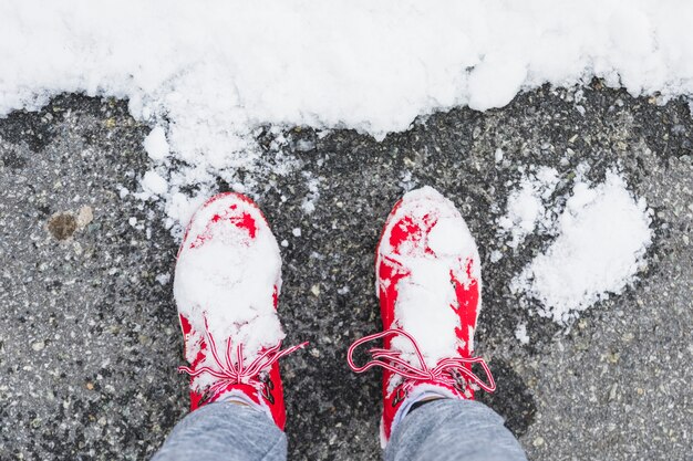 Gambe della persona in stivali su asfalto vicino neve