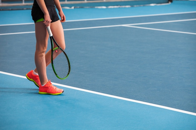 Gambe della ragazza in un campo da tennis chiuso con palla e racchetta