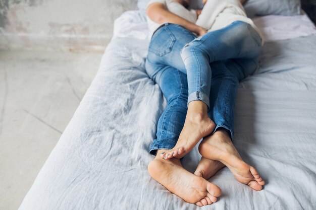 Gambe di giovane coppia sdraiata sul letto a casa in abbigliamento casual, dormire in jeans, uomo e donna che trascorrono del tempo felice insieme, rilassarsi, abbracciare, amore e romanticismo