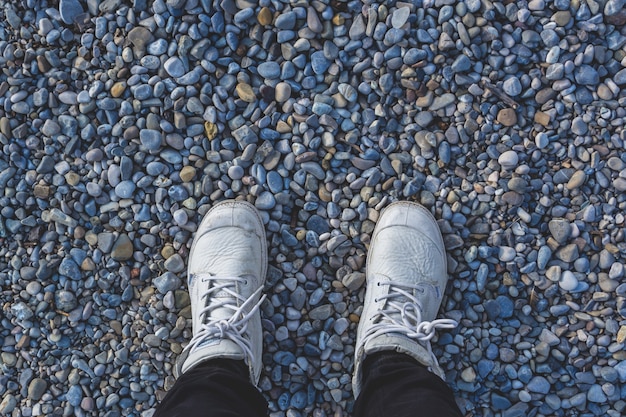 Gambe umane in scarpe da ginnastica bianche in piedi sulla spiaggia sassosa