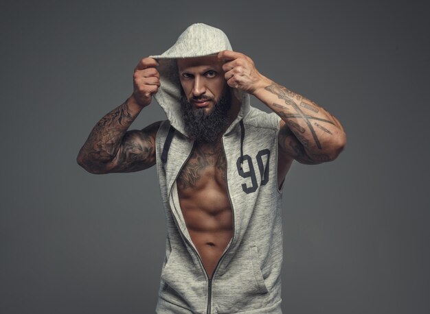 Gangsta ha tatuato un uomo muscoloso con un cappuccio. Isolato su sfondo grigio.