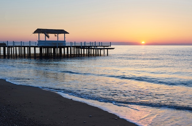 Gazebo sul molo in legno in mare con il sole al tramonto.