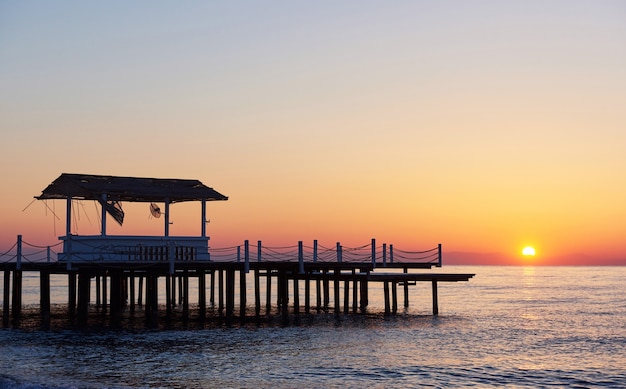 Gazebo sul molo in legno in mare con il sole al tramonto.