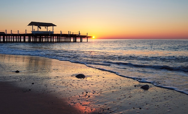 Gazebo sul molo in legno in mare con il sole al tramonto.