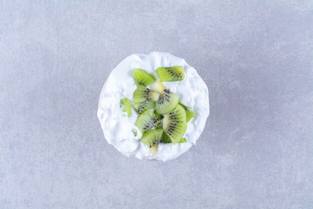 Gelato in un piedistallo di vetro con fette di kiwi sul tavolo di marmo.