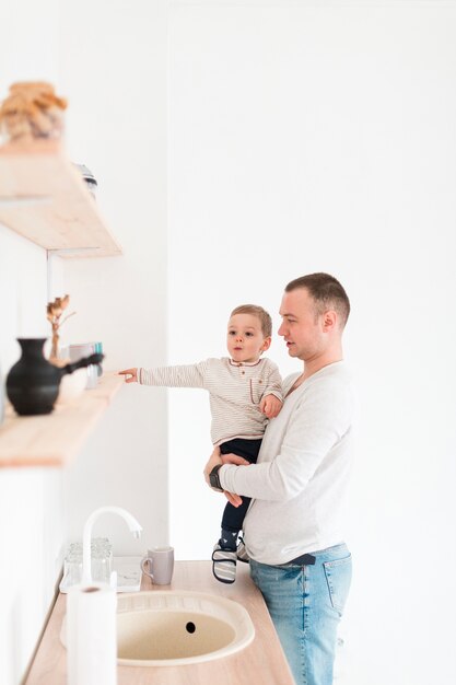 Generi il bambino della tenuta mentre nella cucina con lo spazio della copia