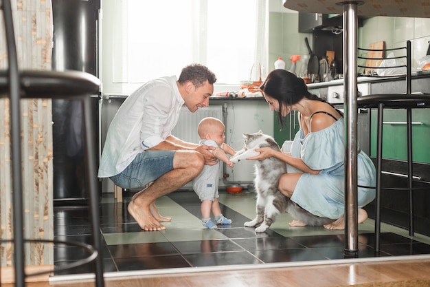 Genitore sorridente che gioca con il gatto e il loro bambino in cucina