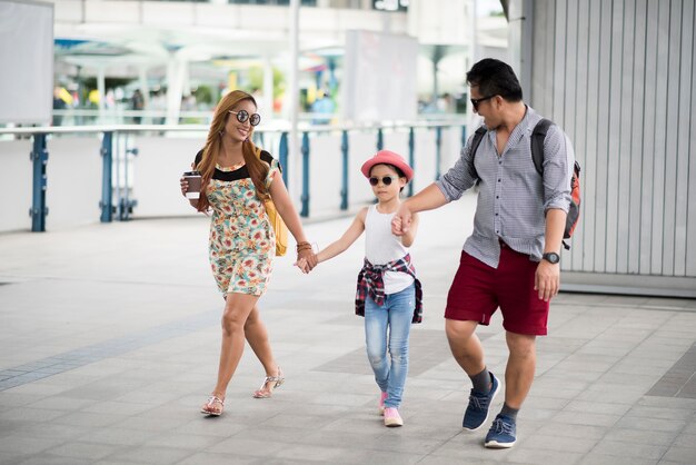 Genitori alla moda felici che si tengono per mano con la figlia che cammina sulla via nella città