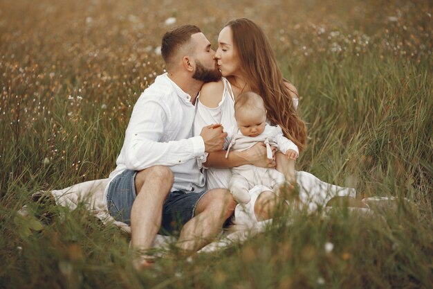 Genitori con figlia. Famiglia in un campo. Ragazza appena nata. Donna in abito bianco.