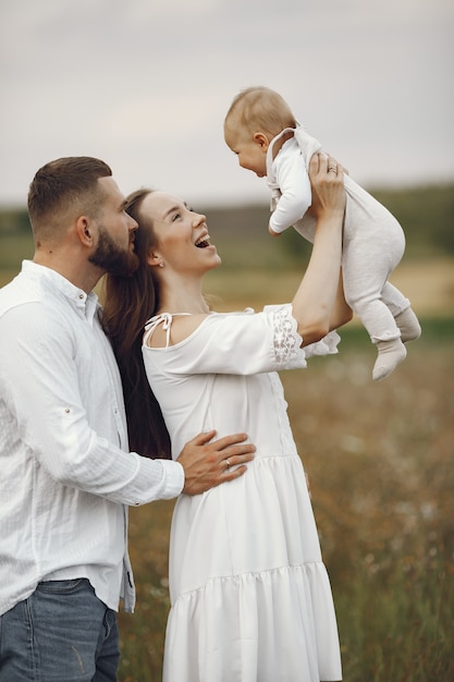 Genitori con figlia. Famiglia in un campo. Ragazza appena nata. Donna in abito bianco.