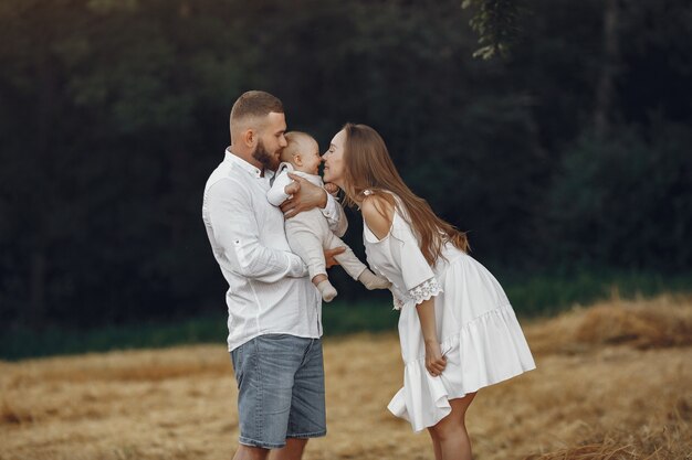 Genitori con figlia. Famiglia in un campo. Ragazza appena nata. Donna in abito bianco.