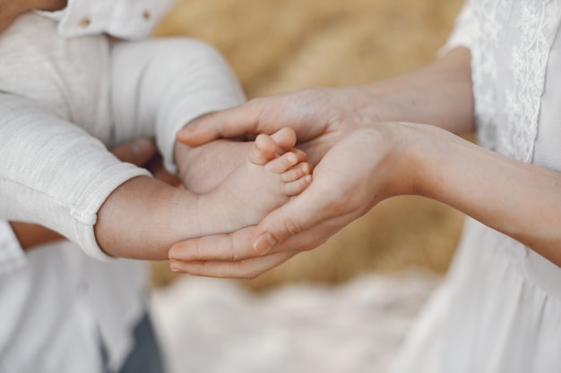 Genitori con figlia. Famiglia in un campo. Ragazza appena nata. Donna in abito bianco.