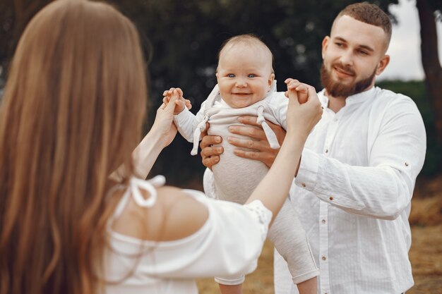 Genitori con figlia. Famiglia in un campo. Ragazza appena nata. Donna in abito bianco.