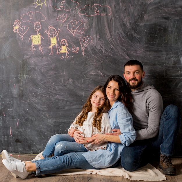 Genitori con la figlia che abbraccia vicino alla lavagna con il disegno