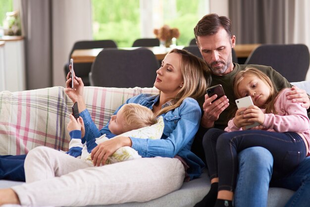 Genitori e figli che usano il cellulare in soggiorno