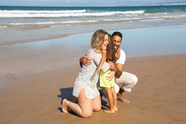 Genitori felici che abbracciano la piccola figlia sulla sabbia bagnata in mare