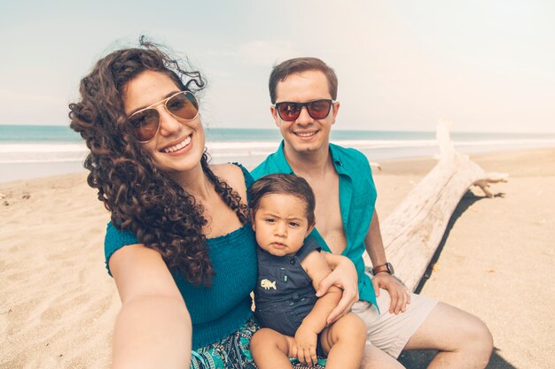 Genitori felici che sorridono e che prendono selfie sulla spiaggia.