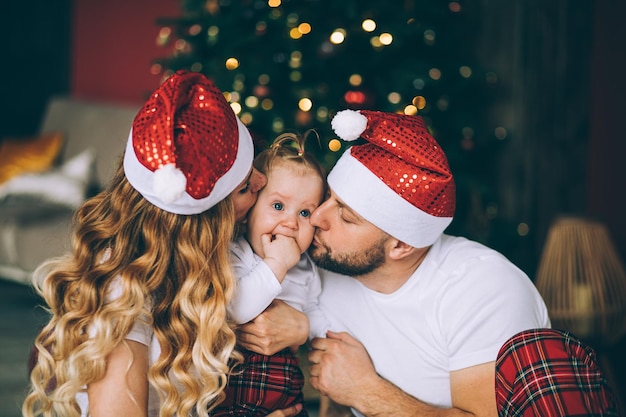 Genitori in cappelli di Babbo Natale che baciano il bambino.