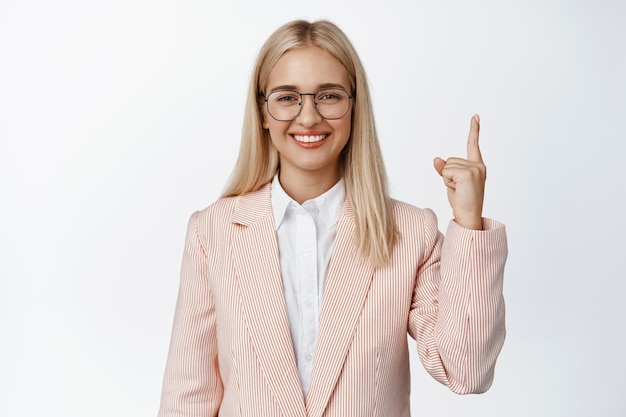 Gente aziendale Commessa professionista in tuta e occhiali sorridente che punta il dito verso l'alto mostrando lo sfondo bianco della pubblicità