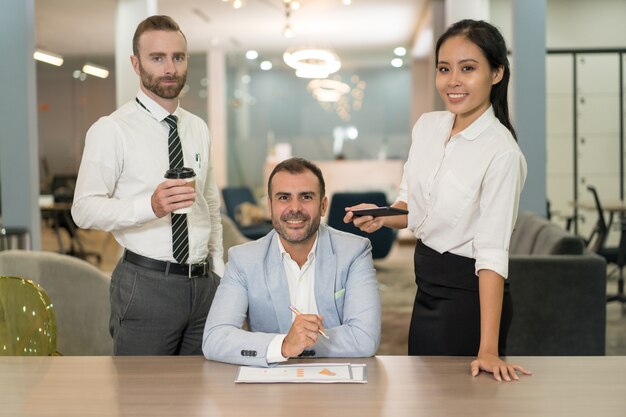 Gente di affari che lavora e che posa allo scrittorio in ufficio