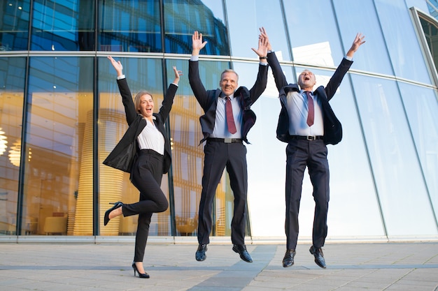 Gente di affari eccitata felice che celebra il successo insieme, saltando e gridando. A figura intera, vista frontale. Squadra di successo e concetto di lavoro di squadra