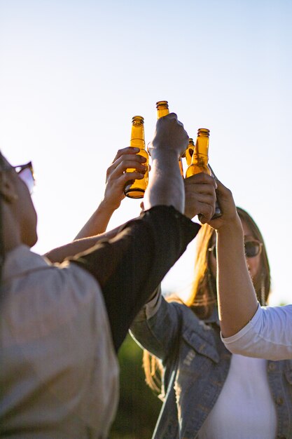 Gente felice che incoraggia con le bottiglie di birra contro il tramonto. Giovani amici rilassati che si rilassano insieme nel parco. Concetto di tempo libero