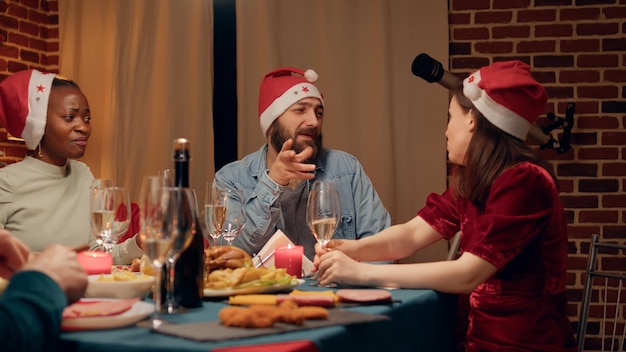 Gente festiva che parla alla cena di Natale mentre si gusta il cibo tradizionale cucinato in casa. Membri gioiosi della famiglia che discutono a casa mentre celebrano insieme le vacanze invernali.