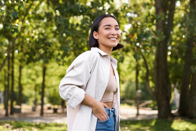 Gente moderna giovane ragazza asiatica felice che cammina nel parco sorridendo e godendosi la bella giornata estiva