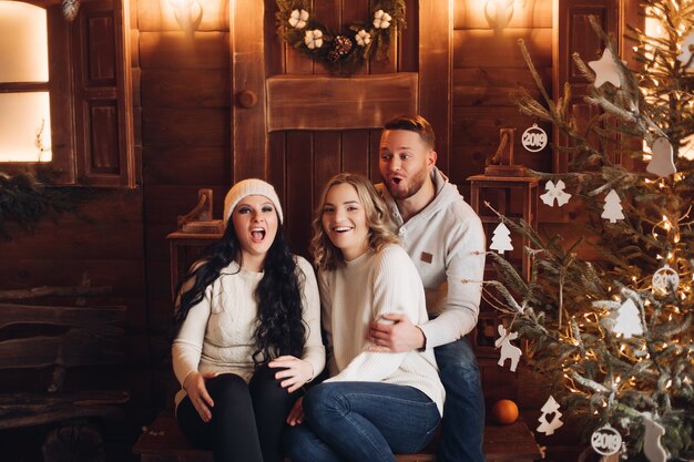 Gente sorridente che si siede sulla veranda in legno davanti alla porta con la corona di Natale