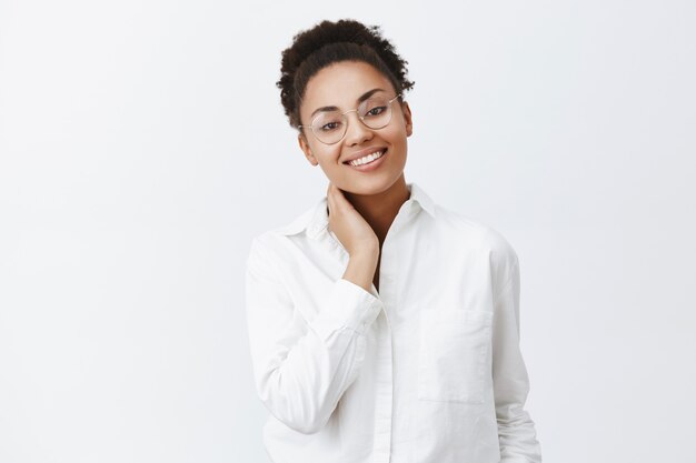 Gentile donna afro-americana in occhiali e camicia, toccando il collo e guardando