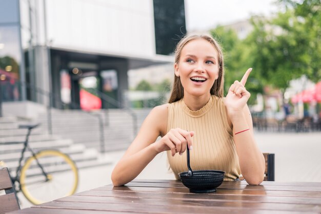 Gesto di giovane bella donna con il dito mentre mangia insalata al caffè all'aperto