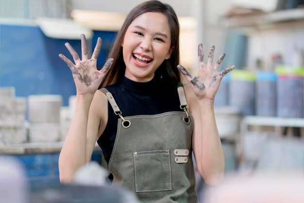 Gesto sorridente saluto l'artista crramist femminile asiatico guarda la fotocamera artista allegro guarda la fotocamera portriat girato mentre scolpisce il suo nuovo lavoro in laboratorio di ceramica studio d'arte e creazione femminile