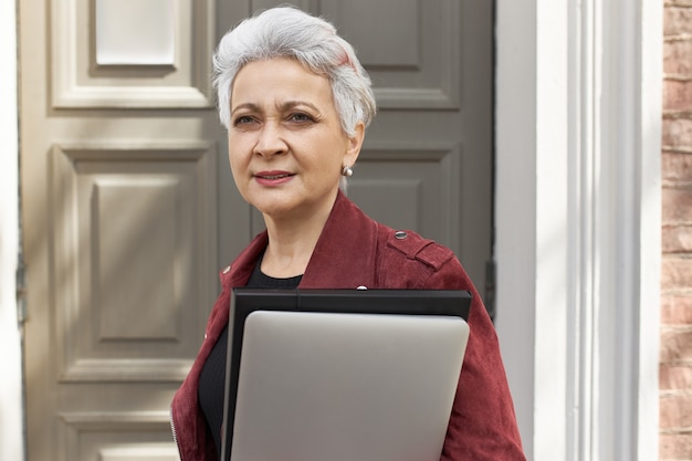 Gestore immobiliare di mezza età fiducioso di successo con laptop che trasporta taglio di capelli corto alla moda