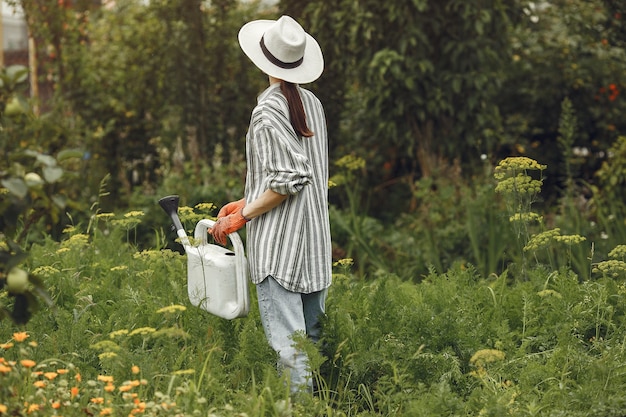 Giardinaggio in estate. Donna che innaffia i fiori con un annaffiatoio. Ragazza che indossa un cappello.